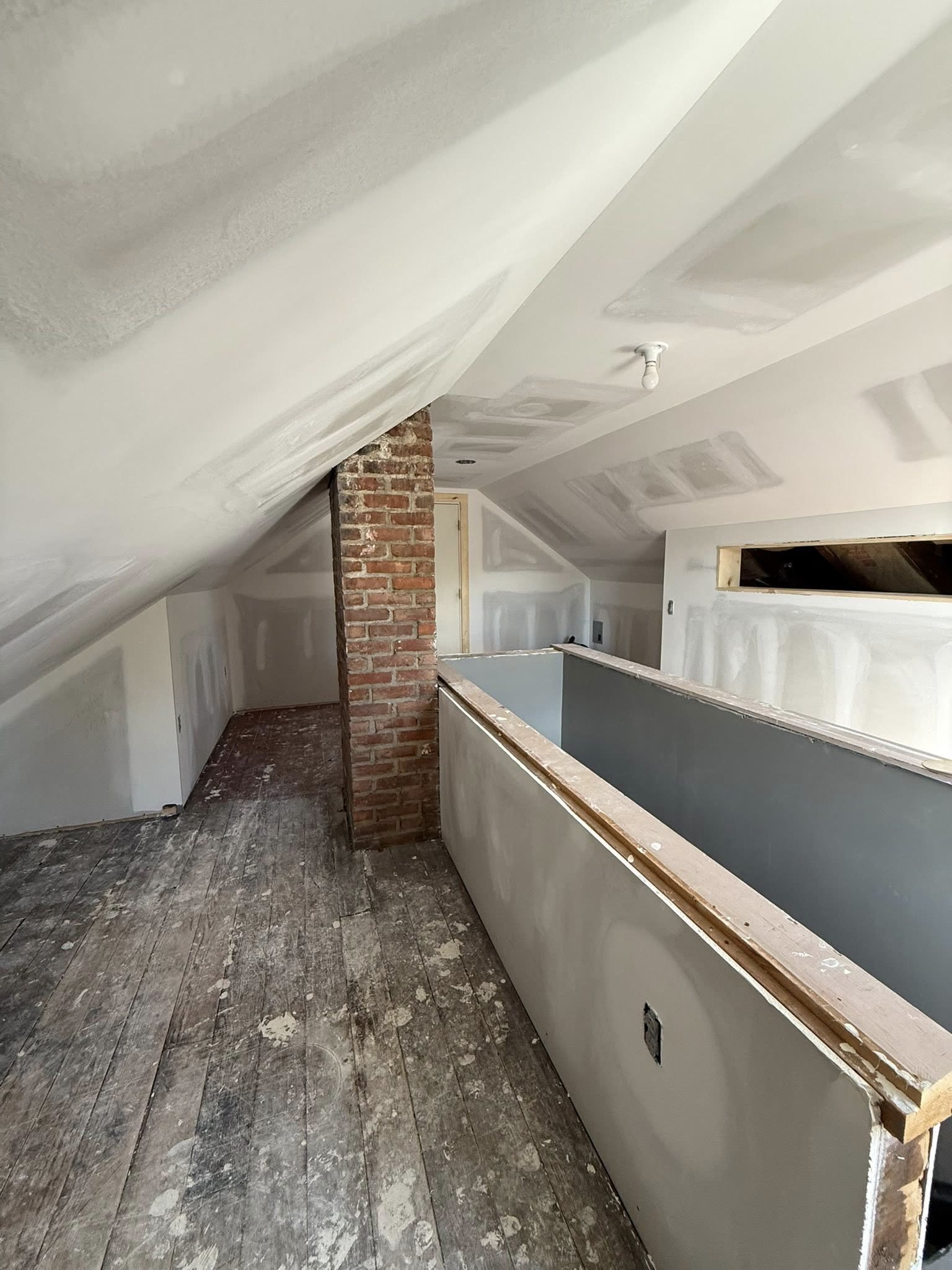 Loft with finished drywall seams on sloped ceilings and a half-wall